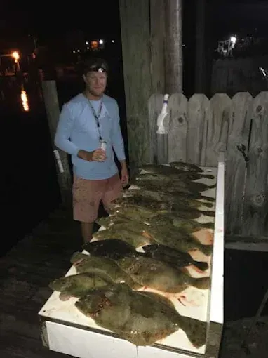 Person standing beside a table covered with many fish at night by the water