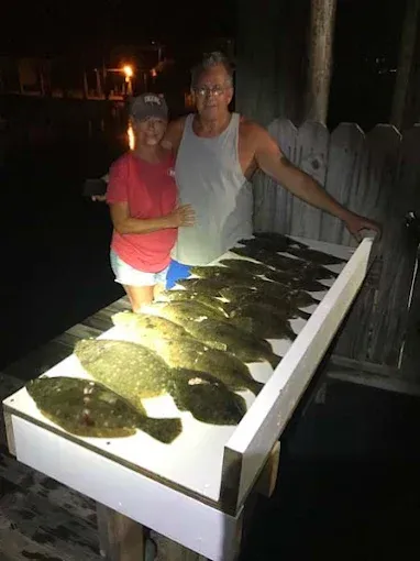 Two people pose beside a table covered with freshly caught fish at night.