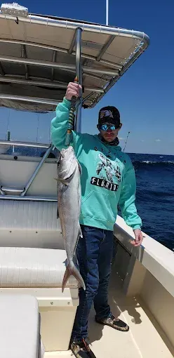 Person on a boat holding up a large fish, wearing a teal hoodie and sunglasses.