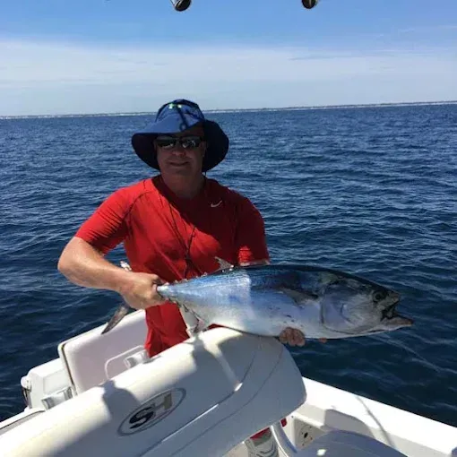 Person in red shirt holding a large fish on a boat at sea under a clear sky