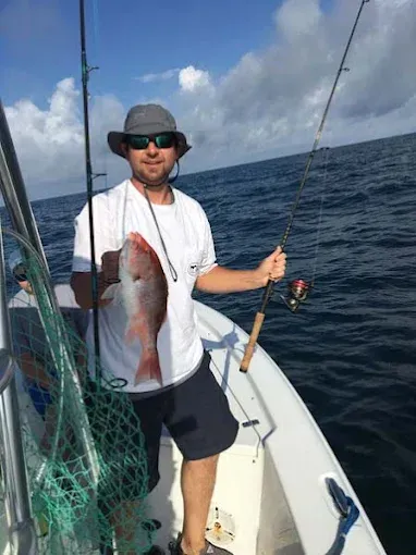 Person on a boat holding a large fish, with fishing gear and open ocean in the background.