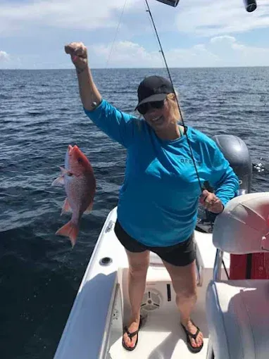 Angler on a boat holds up a red fish over the ocean on a sunny day