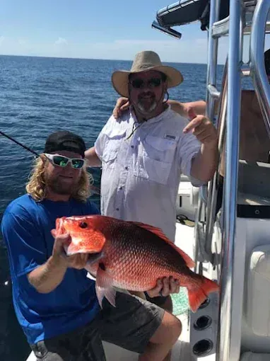 Two anglers on a boat hold up a large red fish on the open sea.