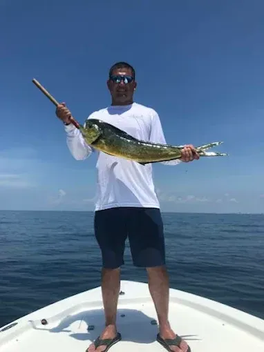 Person on a boat holding a large fish over open water on a clear day