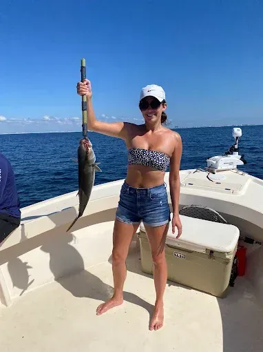 Person on a boat holding up a large fish over blue ocean under a clear sky.