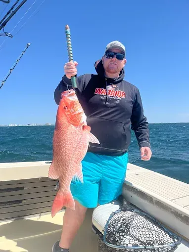 Angler on a boat holds a large red fish beside the ocean.