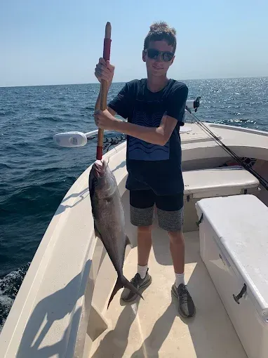 Person on a boat holding a large fish over the ocean