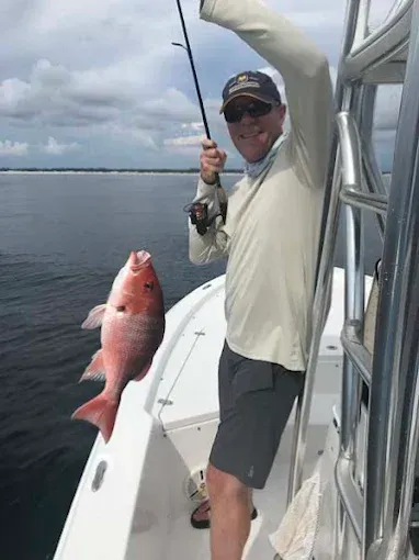 Angler on a boat holding a large red fish over calm water under cloudy skies