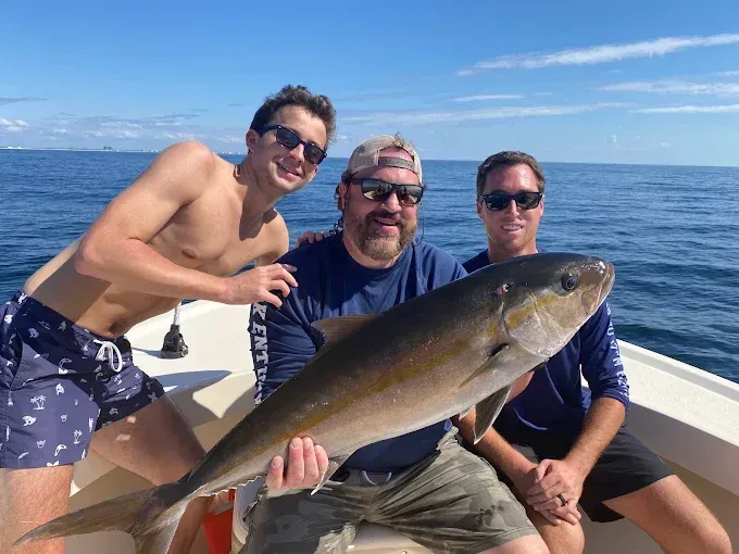 Three men on a boat holding a large fish on the ocean under a clear blue sky