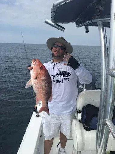 Man on a boat holding a large pink fish, smiling on open water under a cloudy sky