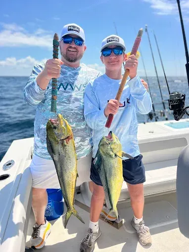 Two anglers on a boat hold up large fish on a sunny day at sea.
