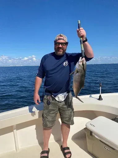 Person on a boat holding up a large fish over the ocean under a blue sky.