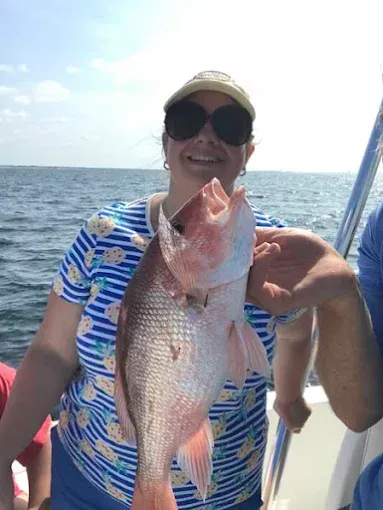 Person on a boat holding up a large pink fish on the ocean