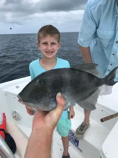 Boy on a boat holding a large fish, with the ocean in the background.