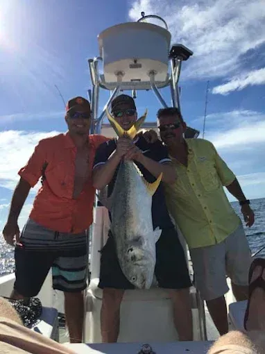 Three people on a boat hold up a large fish under bright sun.
