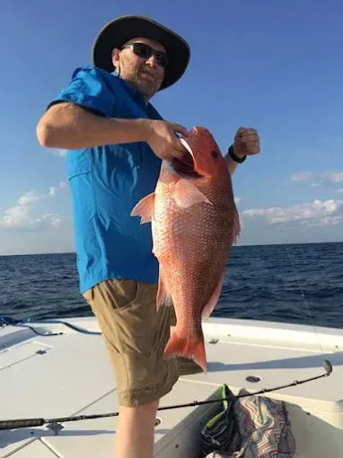Man on a boat holding a large red fish over the ocean under a clear blue sky