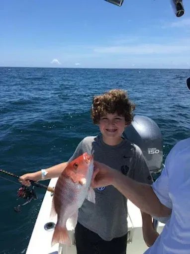 Person on a boat holding a large fish on a sunny ocean.