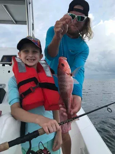 Smiling child on a boat with an adult holding a red fish over the water.