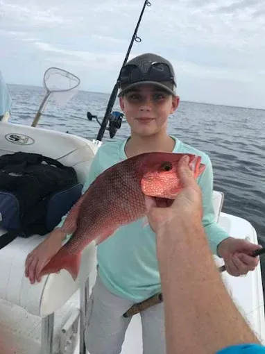 Person on a boat holding a red fish on the open water.