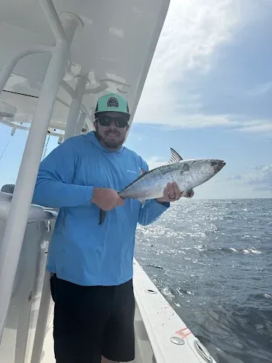 Man holding a fish on a boat deck beside open water under a bright sky