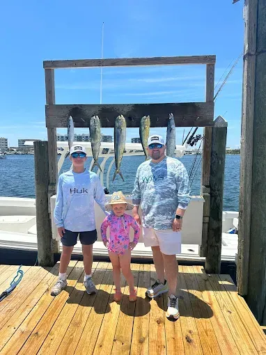 Three people posing with hanging fish on a sunny dock by the water