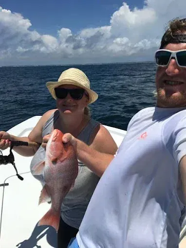 Two people on a boat holding a large fish with the ocean and cloudy sky behind them