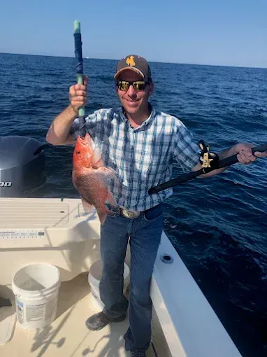 Man on a boat holding two fish and fishing gear on the ocean