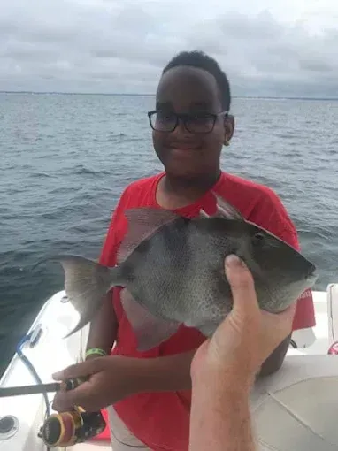 Person on a boat holding a large gray fish on the ocean