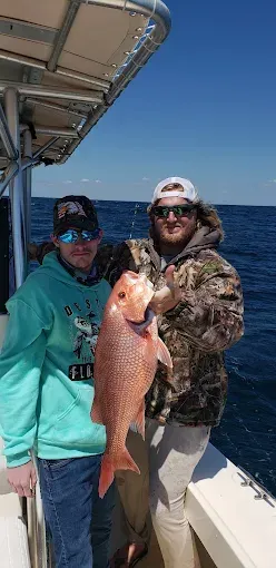 Two people on a boat hold up a large fish with the ocean in the background.