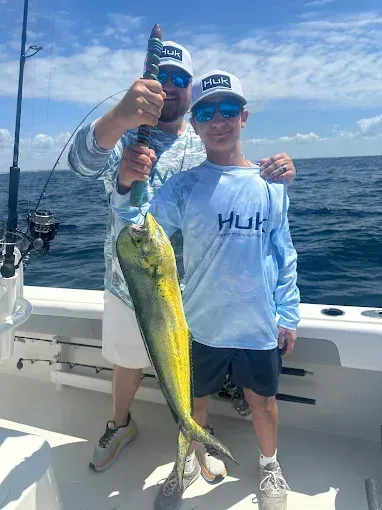Two people on a boat holding a large yellow fish over the ocean under a blue sky.