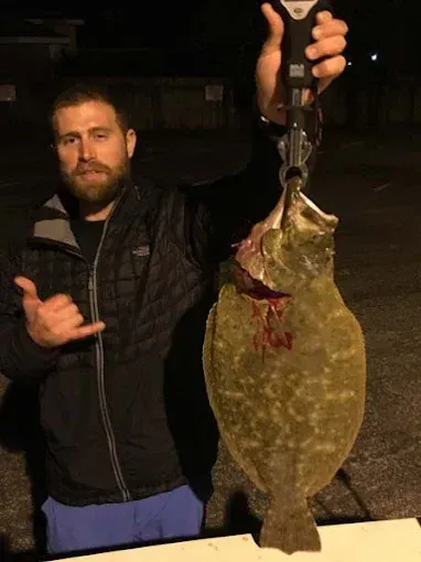 Man holding up a large flat fish by a hook at night on a road.