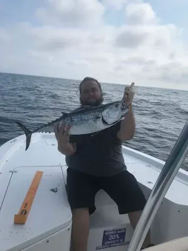 Person on a boat holding a large fish over the ocean under a cloudy sky