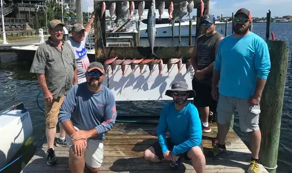 Four people pose on a dock in front of a shark-shaped fishing boat mural.