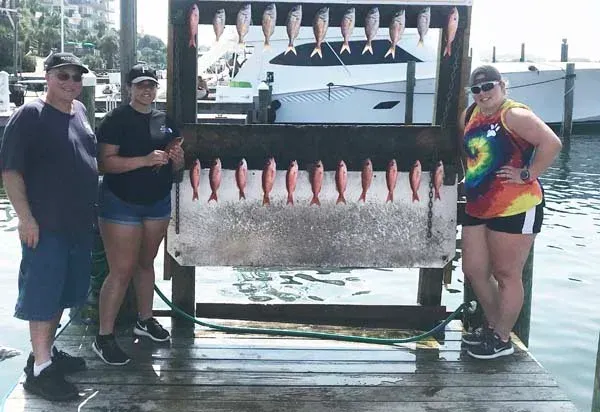 Three people posing beside a fish display board on a dock by the water
