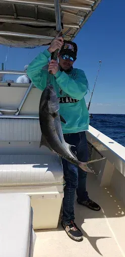 Person on a boat holding a large fish on a fishing line with the ocean in the background