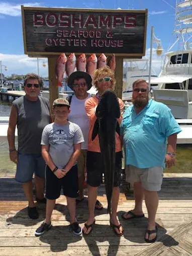 Five people posing in front of a Bojangles seafood and oyster house sign at a marina.