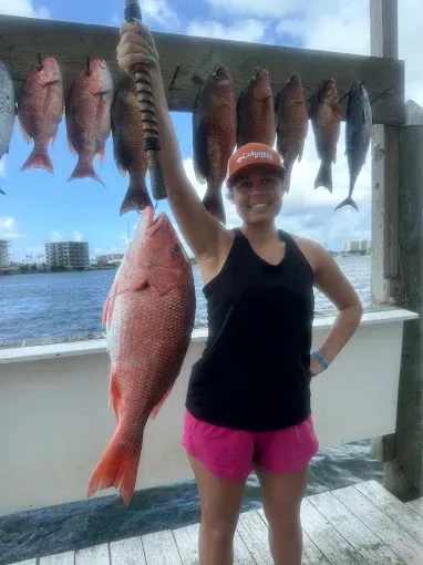 Woman holding a large fish on a dock with several fish hanging behind her over the water