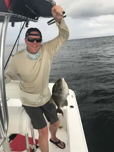 Person holding up a large fish on a boat at sea, wearing sunglasses and a cap.