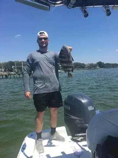 Man standing on a boat deck holding a large fish on a sunny lake.