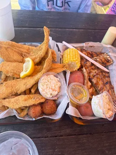 Two takeout seafood platters with fried fish, shrimp, fries, and lemon wedges on a table