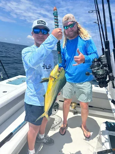 Two anglers on a boat hold a large yellow fish, smiling on a sunny day at sea