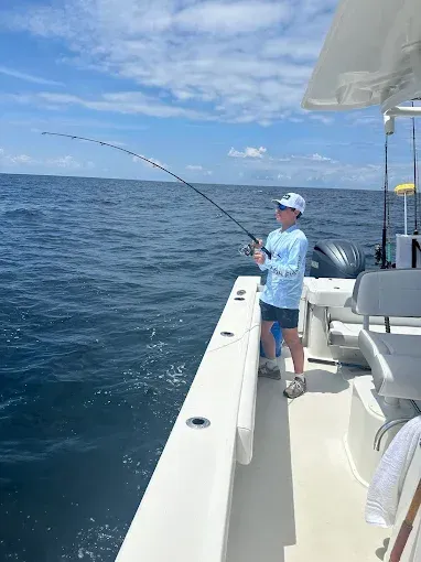 Person fishing from a boat on blue ocean under a partly cloudy sky