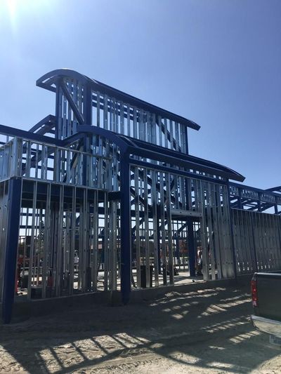 Metal playground climbing structure under a bright blue sky, with strong shadows on the ground.