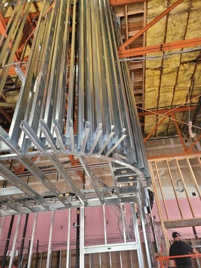 Construction site with exposed metal ductwork and framing, plus yellow insulation and scaffolding overhead