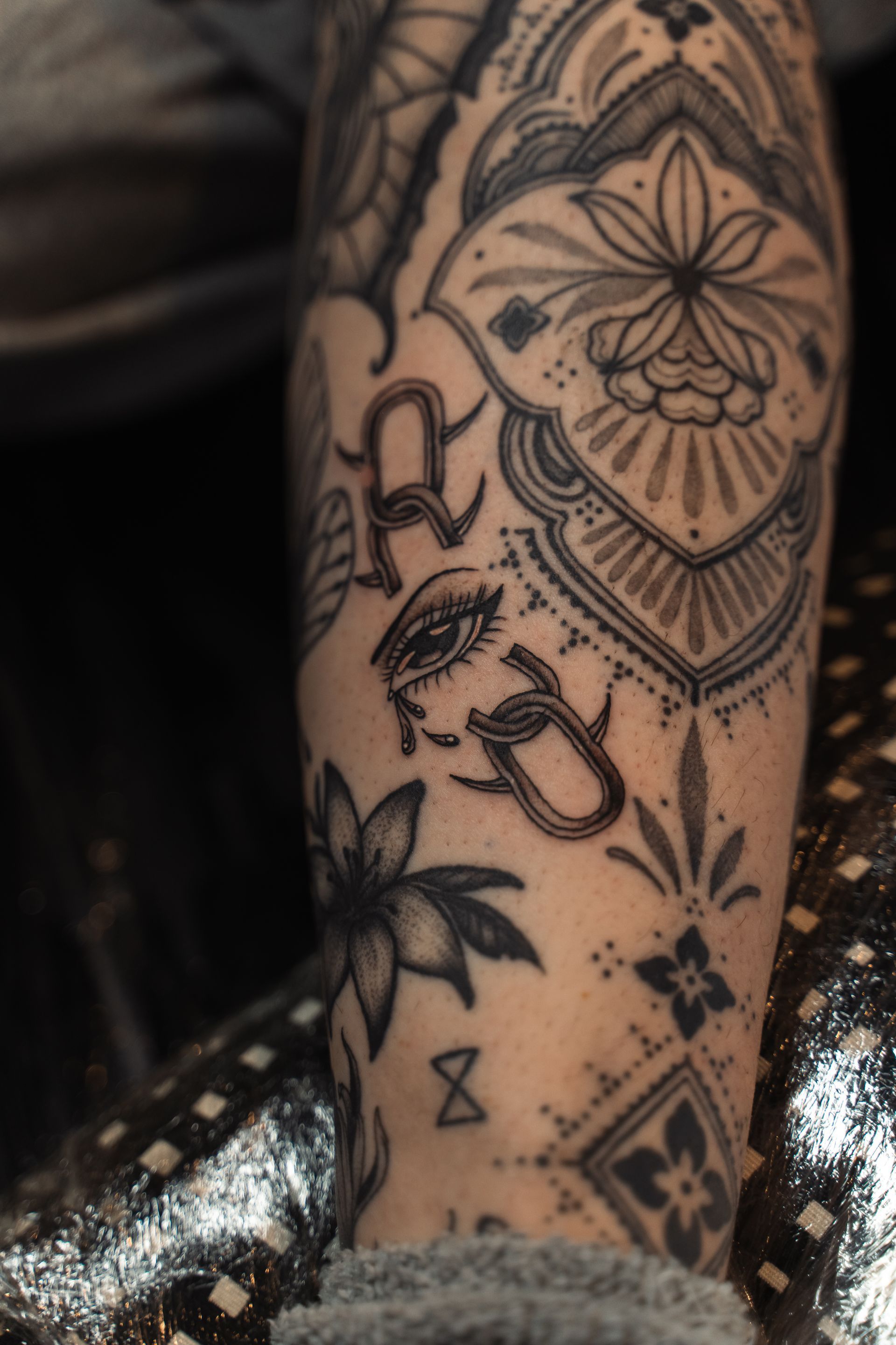 Tattooed arm with floral and geometric black ink designs on a dark, patterned background