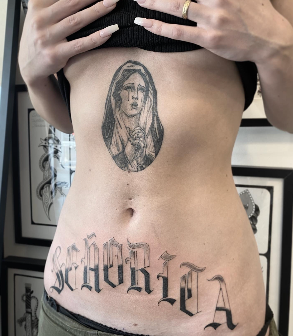 Torso with a religious chest tattoo and large gothic script tattoo across the lower abdomen.