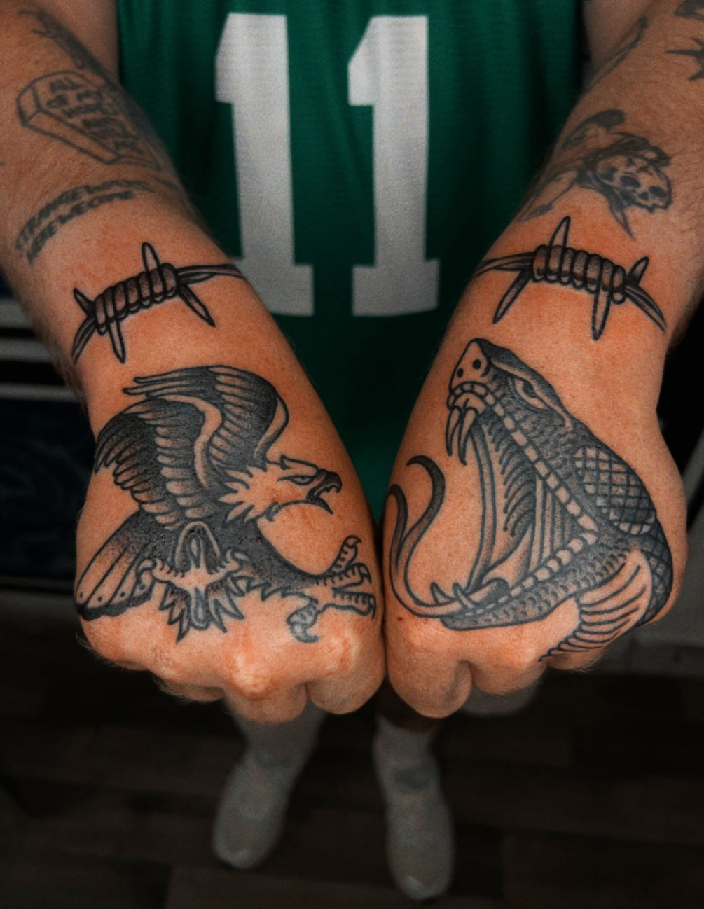 Tattooed fists held together, showing black ink designs against a green jersey with number 11