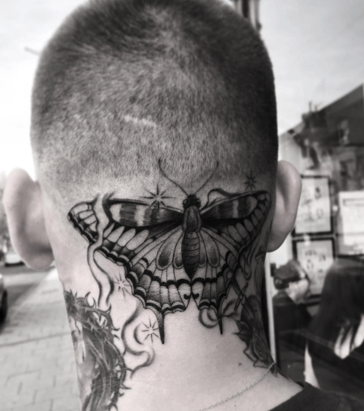 Back of a shaved head with a large butterfly tattoo across the neck and nape