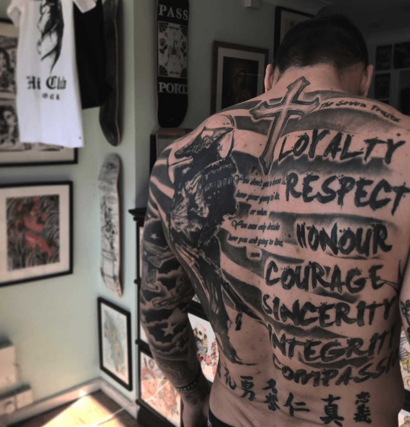 Tattooed back with bold black script and graphic tattoo art in a framed indoor room