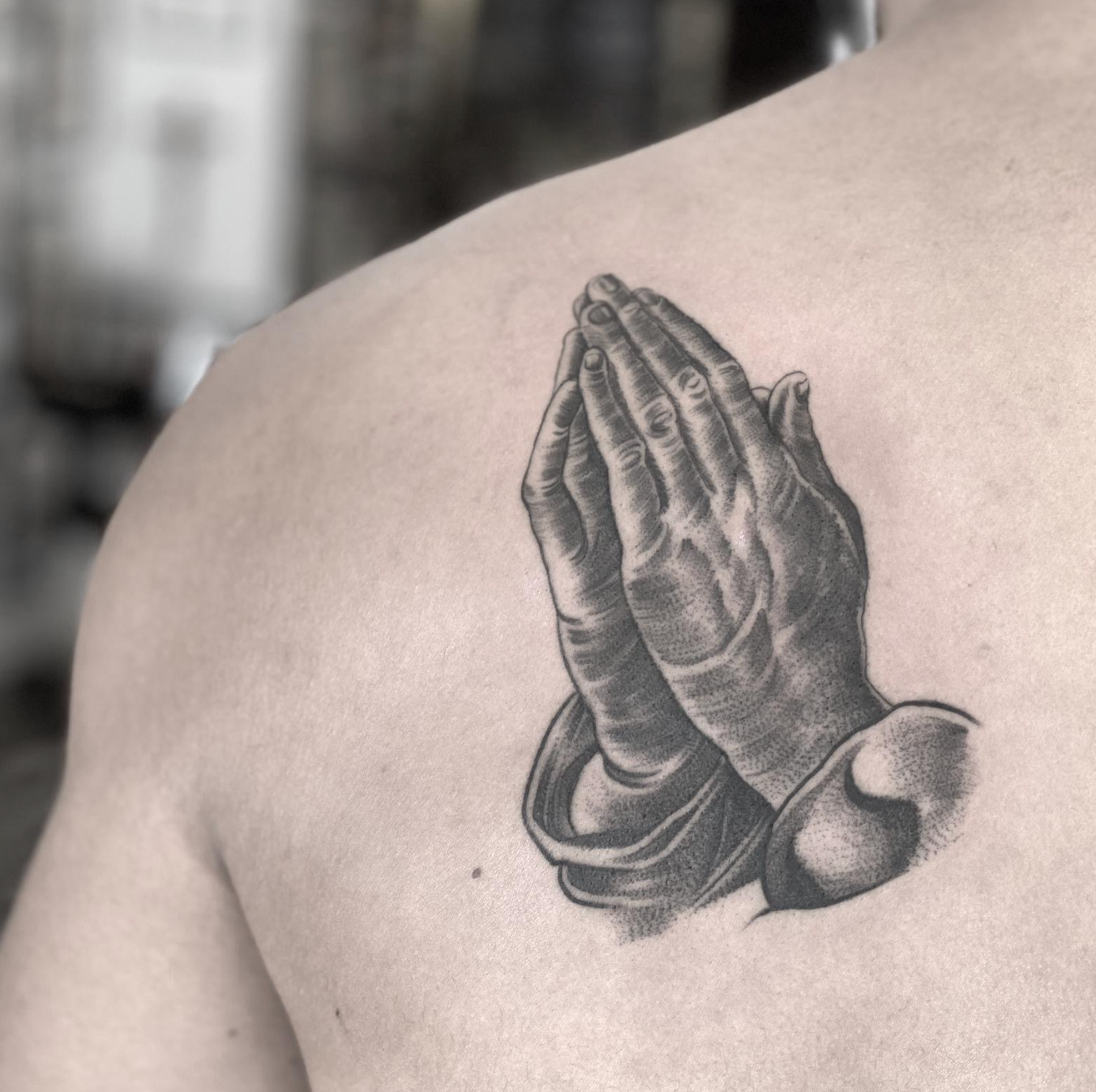 Black-and-gray praying hands tattoo on an upper back/shoulder